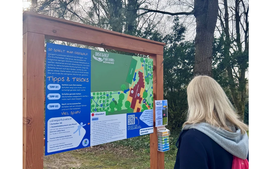 Person liest Informationstafel mit Tipps & Tricks am Discgolf-Parcours Möhnesee