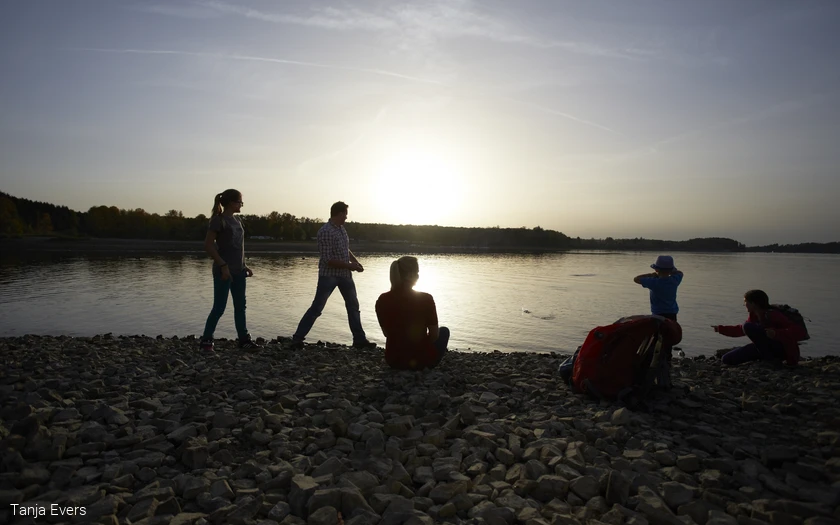 Silhouetten von Personen an einem Seeufer bei Sonnenuntergang.