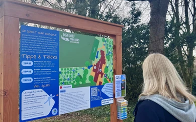Person liest Informationstafel mit Tipps & Tricks am Discgolf-Parcours Möhnesee